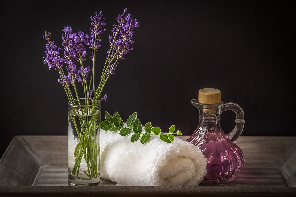 A glass with fresh lavender, a bath towel, and a small crystal flagon with a pink liquid.